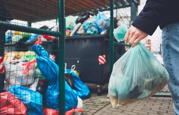 person holding trash bag full of trash to the trash bin